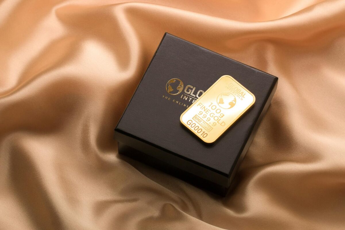 A pristine gold bar resting on a luxurious black box atop a smooth silk fabric.